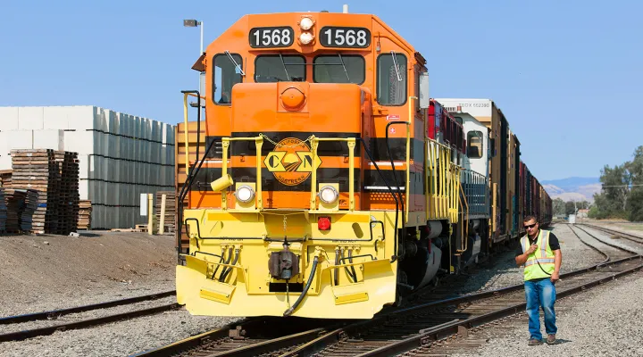 Train pulling freight railcars with a G&W employee next to the train in a railroad yard