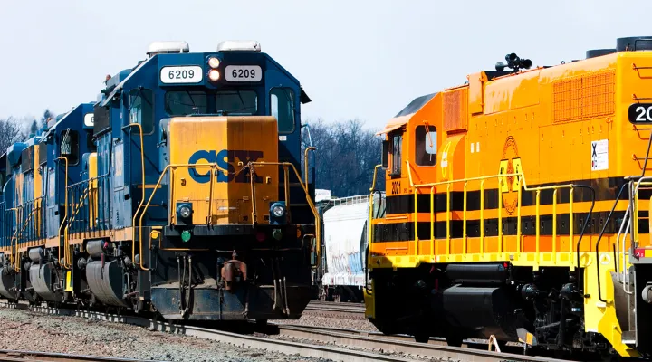 An orange Genesee & Wyoming train on the right and a navy and orange CSX train on the left