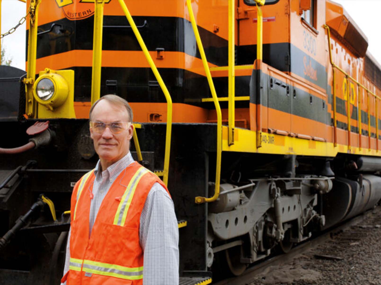 Mortimer B. Fuller III wearing safety glasses and a safety vest standing in front of a train