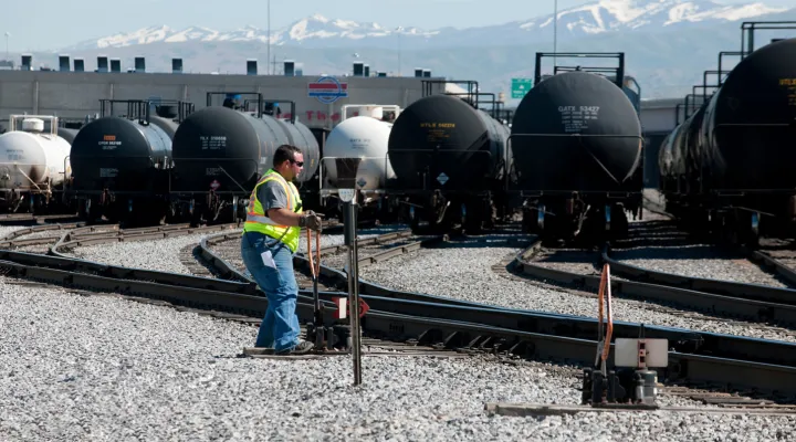 G&W employee wearing a high-visibility vest and sunglasses moving a track's direction in a railroad yard filled with tank cars