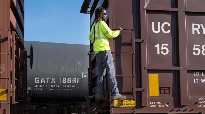 G&W employee in a high-visibility jacket standing on a ladder on a freight train car