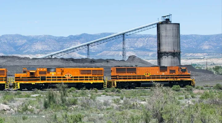Train traveling in a desert with a large industrial tower in the background