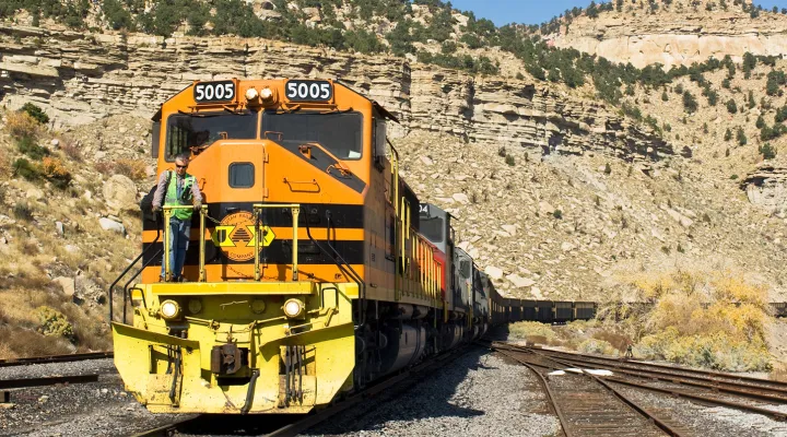 Train pulling freight railcars through the desert with a G&W employee standing at the head of the train