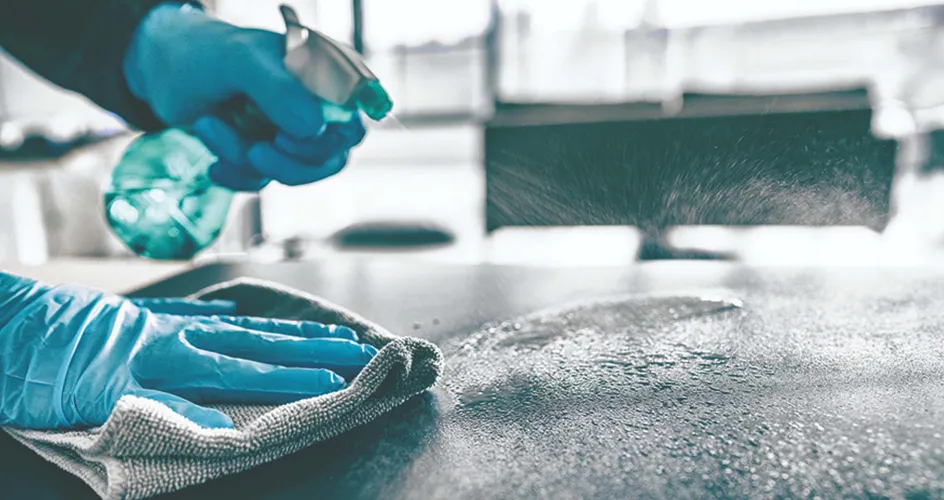 Person with blue cleaning gloves, a rag, and spray bottle cleaning tabletop surface